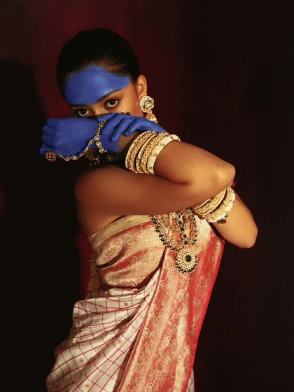 A mysterious and artistic pose, where the blue-painted hands partially obscure the model's face. This shot plays with concealment and revelation.