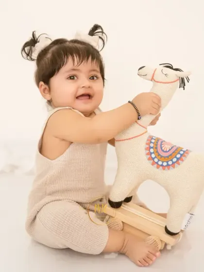 A happy toddler plays with a rocking llama toy, creating a fun and interactive photo opportunity.