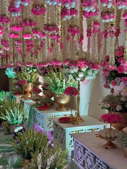 A beautiful composition of floral arrangements on intricately carved white tables. The ceiling of hanging flowers creates a sense of being in a magical, blooming garden.