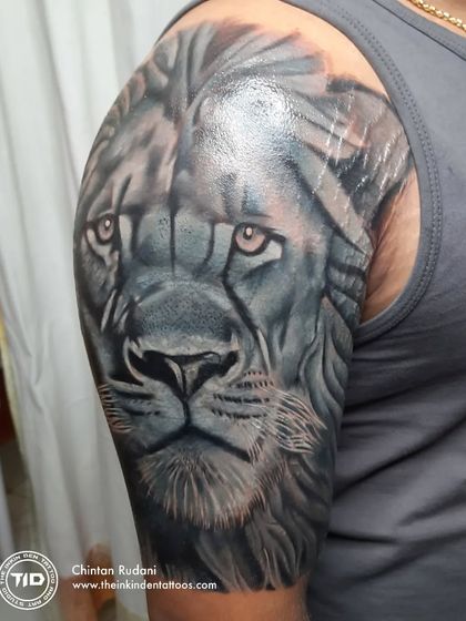 A powerful lion face cover-up tattoo on the shoulder. The deep grey tones and intense eyes completely obscure the old tattoo, replacing it with a symbol of strength and majesty.
