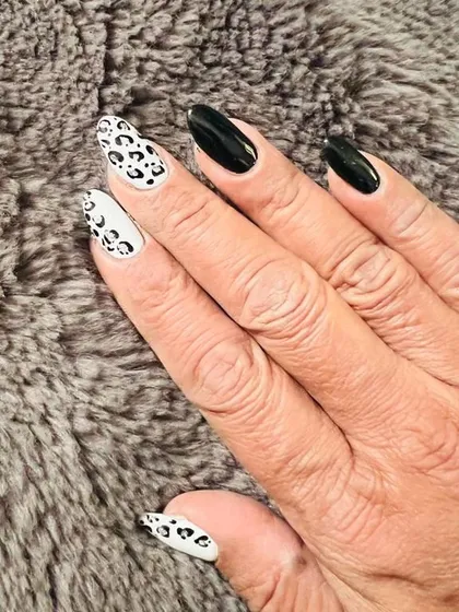 A striking and bold manicure featuring stiletto-shaped nails with a mix of solid glossy black and a contrasting white and black leopard print design.
