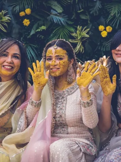 The bride and her friends show off their turmeric-covered hands to the camera during a joyful haldi ceremony.