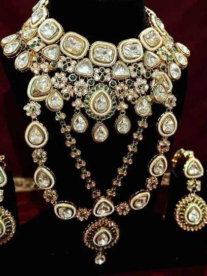 This is a grand, multi-layered Kundan necklace set with green stone accents. It includes a choker and a longer necklace for a complete, royal look.