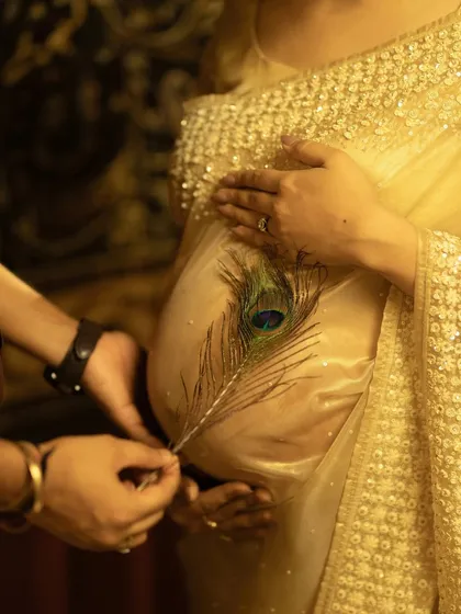 A symbolic and delicate touch. A peacock feather, a symbol of grace and divinity, is gently placed on the baby bump, adding a layer of cultural meaning and beauty to this traditional maternity portrait.