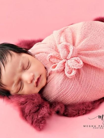 A full-body shot of a newborn in a pink flower-style wrap, resting on a plush, fuzzy surface.