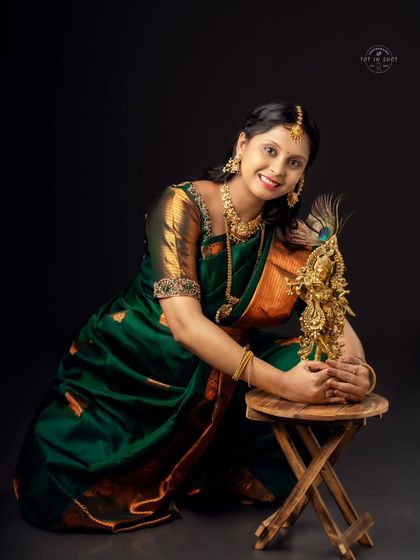 A joyful portrait of a mom-to-be in a traditional green saree, posing with a beautiful brass statue of Lord Krishna.