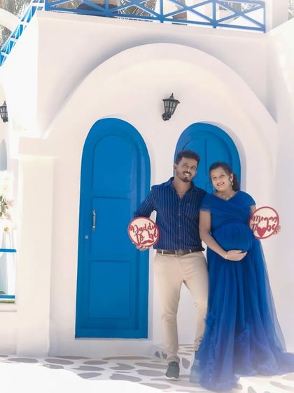 A fun couple's portrait at the Santorini set, holding "Daddy to be" and "Mommy to be" signs. It's a cheerful way to announce your pregnancy with a unique backdrop.