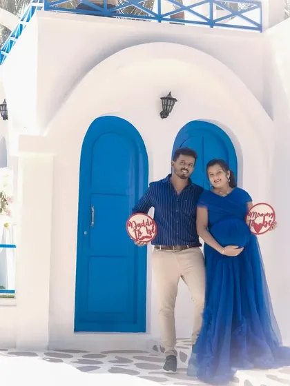 A fun couple's portrait at the Santorini set, holding "Daddy to be" and "Mommy to be" signs. It's a cheerful way to announce your pregnancy with a unique backdrop.