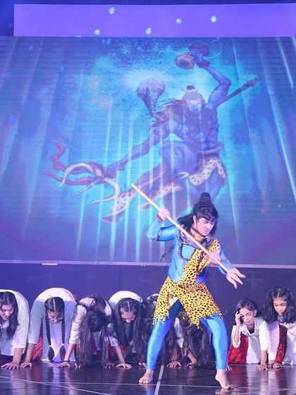 A powerful pose from our Shiv prayer dance. The lead dancer, portraying Lord Shiva, is surrounded by performers in a reverent formation, with a dynamic visual on the screen behind them.