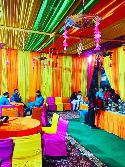 Inside the tent, guests are seated at colourful tables under a canopy of orange, yellow, and green drapes.