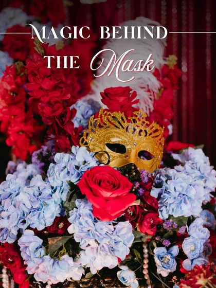 The magic behind the mask. This centerpiece, featuring a golden mask nestled in red and blue florals with pearl and feather accents, perfectly captured our luxurious Masquerade theme.
