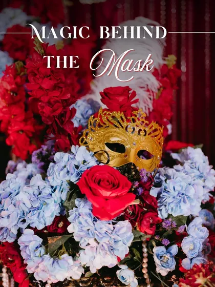 The magic behind the mask. This centerpiece, featuring a golden mask nestled in red and blue florals with pearl and feather accents, perfectly captured our luxurious Masquerade theme.