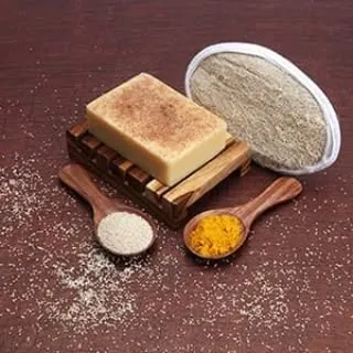This styled shot features a bar of soap on a wooden dish, surrounded by ingredients like turmeric and rice powder, to tell a story about the product's natural composition.