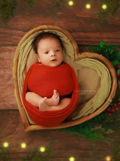 Getting into the festive spirit with a Christmas-themed newborn shoot. The baby is wrapped in red and placed in a heart-shaped bowl with subtle holiday greenery and lights.