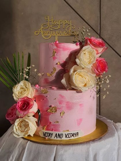 A lovely two-tier anniversary cake in shades of pink, decorated with fresh pink and white roses and a touch of gold leaf. This design is perfect for celebrating love with elegance.
