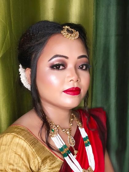 A stunning traditional Assamese bridal look. The makeup is bold with defined eyes and a classic red lip, paired with traditional jewelry.