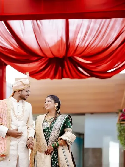 A beautiful shot of the couple walking hand-in-hand under a red draped entrance, creating a grand and colorful frame.