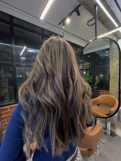 A preview of future trends with this lived-in brunette balayage. The placement of highlights creates a beautiful, flowing effect on long, wavy hair.