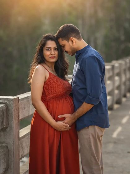 An intimate outdoor couple's portrait on a bridge. The husband-to-be leans in close as they both hold her belly, their expressions full of love and anticipation.