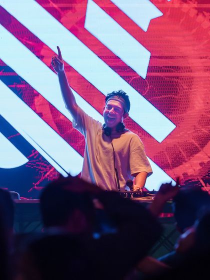 Pointing to the sky, a classic DJ pose to hype up the crowd.