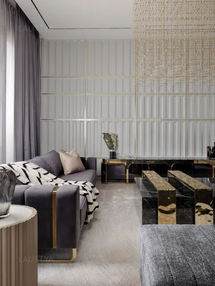 A closer view of the living area, focusing on the interplay of textures. A plush grey sofa with a patterned throw sits before a black marble coffee table, with a fluted side table and a textured wall panel with brass inlays completing the scene.