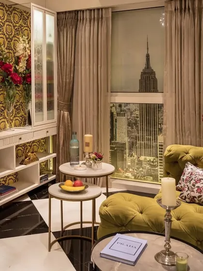 An art-filled, modern living room that exudes opulence. The design features bold patterned wallpaper and luxurious fabrics, creating a glamorous space with a playful, photoshopped view of a city skyline.