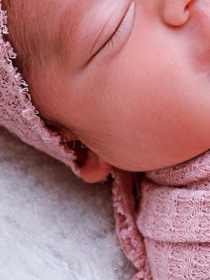 This close-up captures the profile of a sleeping baby, showing the curve of their cheek and the soft texture of the pink swaddle against their skin.