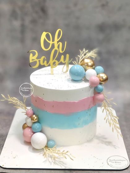 A beautiful baby shower cake with pink, blue, and white stripes. The design is finished with a cascade of colorful spheres and dried wheat stalks.