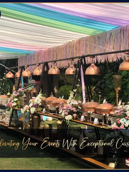A vibrant outdoor buffet under a colorful draped canopy. The copper-toned hanging lamps and serveware create a warm, festive atmosphere perfect for a daytime wedding or celebration.