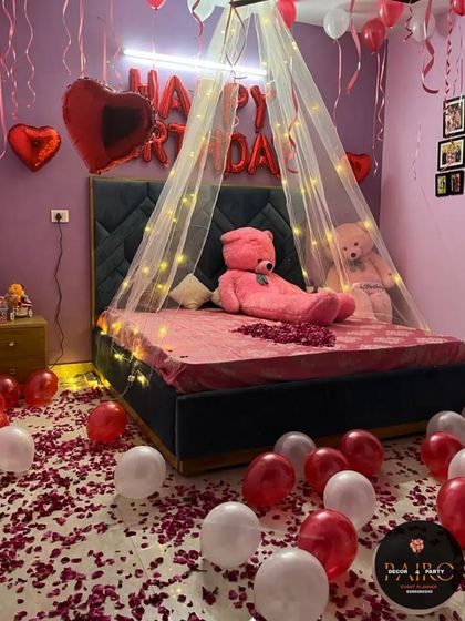 A beautiful canopy decoration for a birthday surprise, with fairy lights, balloons, and rose petals on the bed.