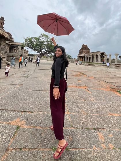 A traveler with an umbrella posing at the Vittala Temple complex in Hampi.