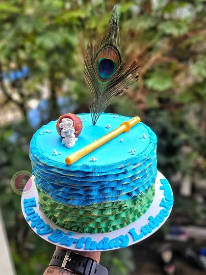 A simple Janmashtami-themed cake with a beautiful ruffled frosting effect in shades of blue and green.