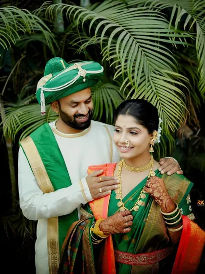 A sweet moment between the couple, captured outdoors against a lush green backdrop. The groom has his arm around his bride, both dressed in beautiful matching green traditional outfits.