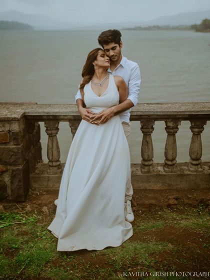 A full-length portrait of a couple in coordinated white outfits, sharing a quiet moment by the water. This showcases a classic, timeless pre-wedding photography style.