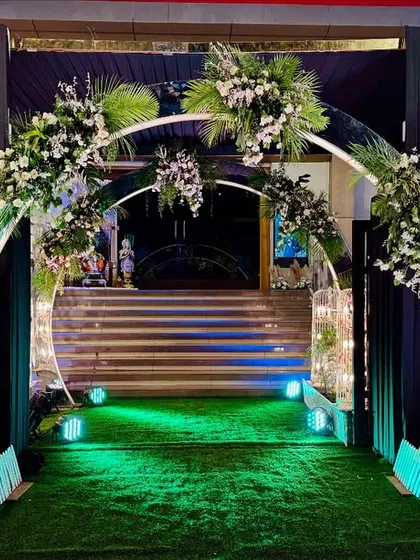 A grand entrance for a black and gold themed Sangeet. The circular arch is adorned with white florals, flanked by structures holding elegant chandeliers, setting a tone of modern luxury from the moment guests arrive.