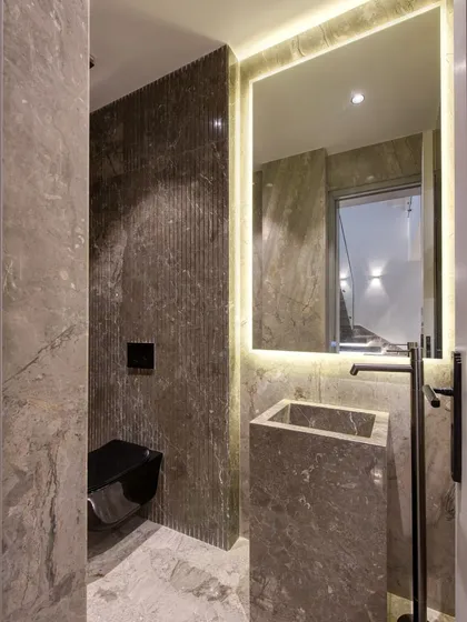 A powder room that exudes modern elegance, with a freestanding pedestal sink carved from a single block of stone and a large, back-lit mirror that provides a soft glow.