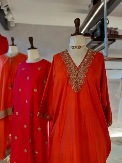 A close-up of a vibrant orange-red kaftan with a beautifully embroidered V-neck, paired with a statement choker.