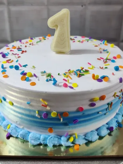 A classic first birthday cake with rainbow sprinkles. The blue ombre effect on the side adds a modern touch.