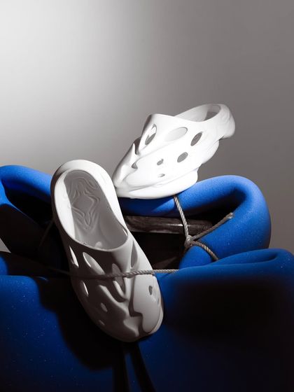 A moody, high-contrast shot of white foam clogs. The dramatic lighting highlights the unique shape and cut-outs of the shoe, giving it an edgy, futuristic feel.
