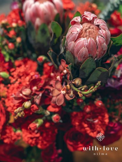 A close-up of a floral arrangement, showcasing the rich textures and deep red hues of the proteas and roses. These flowers were chosen for their dramatic and timeless appeal.