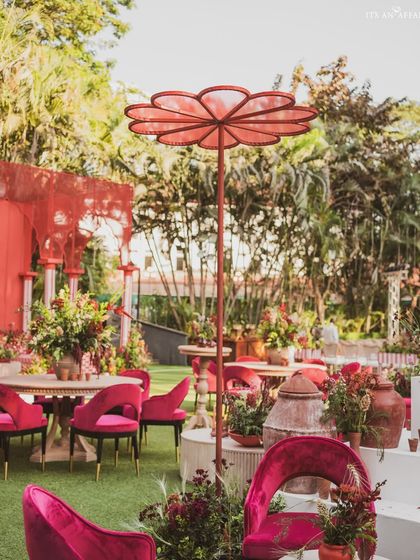 A custom-designed floral-shaped umbrella provides shade for a chic seating area with vibrant magenta velvet chairs.