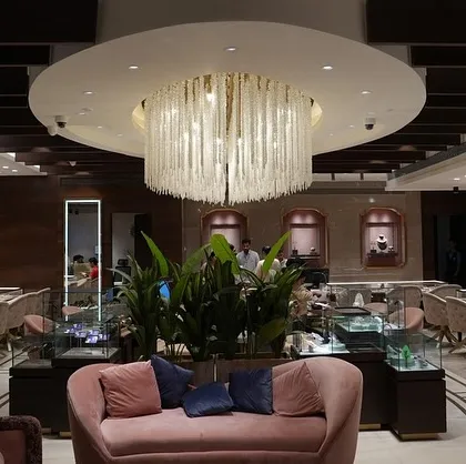 The central lounge area at Batukbhai Jewellers, designed as a luxurious focal point. A magnificent custom chandelier hangs above a plush pink sofa, creating an inviting space for clients to relax while surrounded by elegant displays.