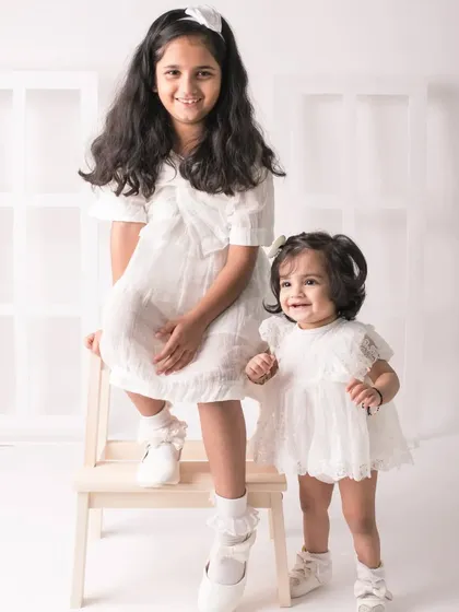 A proud big sister stands by her little sister. The height difference and their sweet interaction make this a charming portrait.