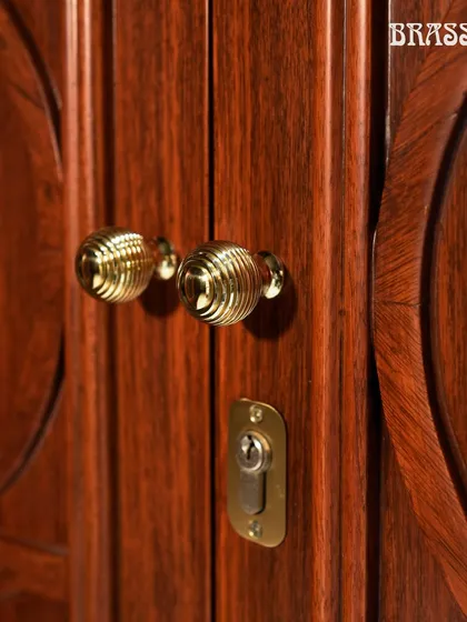 A close-up of the Beehive knobs on the carved wooden cabinet doors, showcasing their intricate design and warm polished brass finish.
