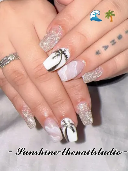 Beach-ready nails. This set combines silver glitter with accent nails featuring hand-painted palm trees against a white background.