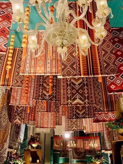 A view looking up at the stunning ceiling installation of hanging rugs and crystal chandeliers, a testament to creative and bold decor choices.