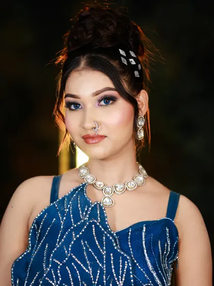 A stunning party look with a high bun and smokey eyes, created for a portfolio shoot. The model is wearing a modern, embellished blue gown.