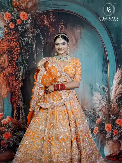 A full-length view showcasing the magnificent orange lehenga against a beautiful floral backdrop. The entire look is a celebration of color, tradition, and bridal joy.