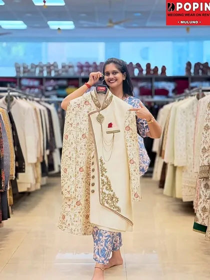 This is a classic groom's sherwani, one of my most popular rental items. It features intricate floral embroidery on an ivory base with a matching stole and a royal chain accessory, offering a complete, regal look.
