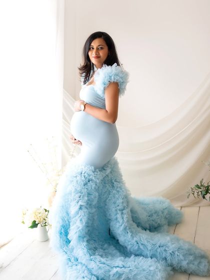 A full-length shot showcasing the magnificent trail of the ruffled blue gown. The simple, bright background makes the color and texture of the dress pop.